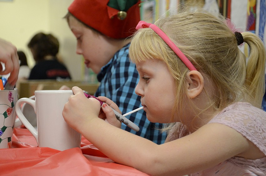 Tesla Johnson draws  on a mug at a craft table.