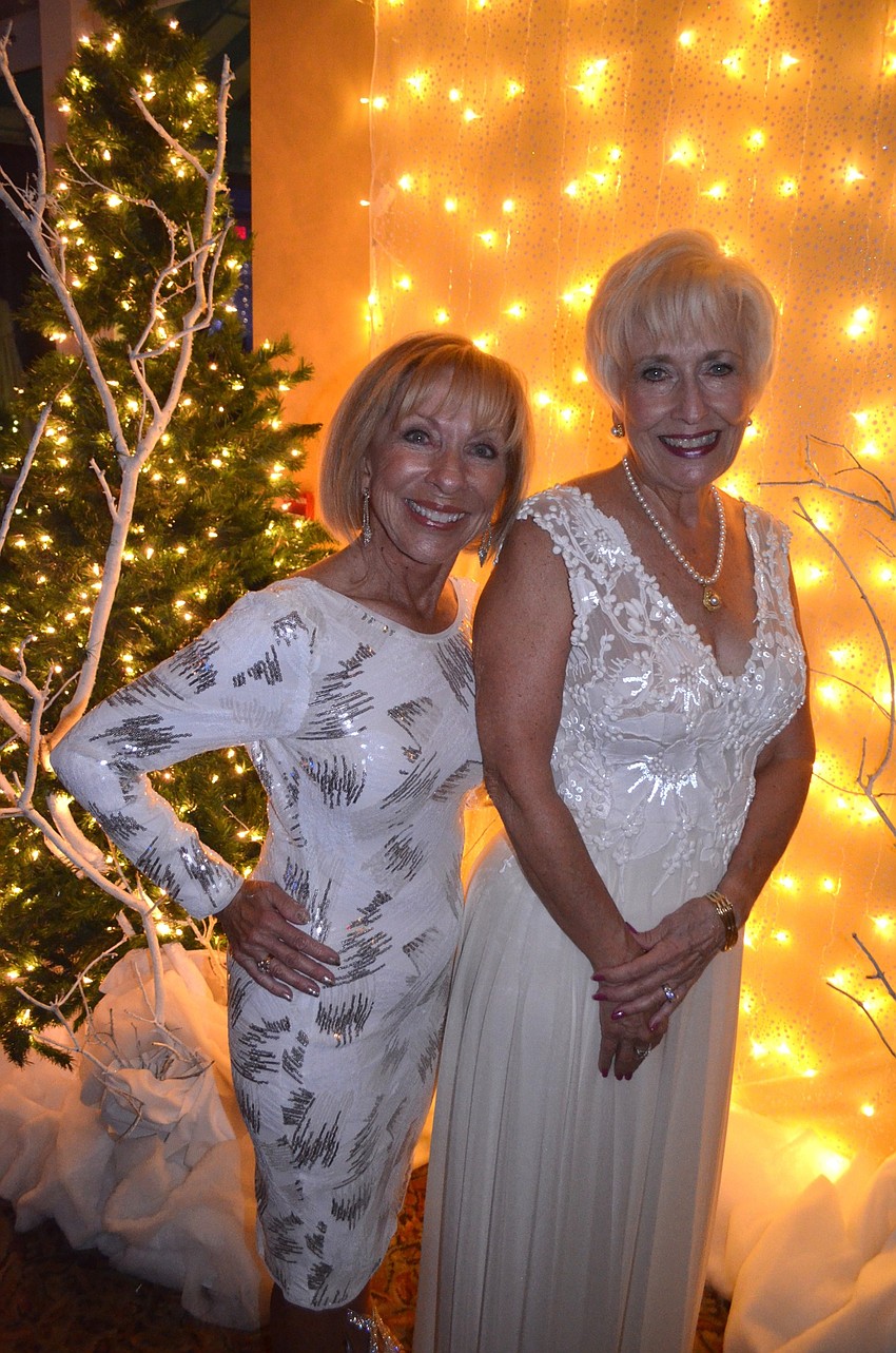 Event Chairwoman Evelyn Cooper and Women's Club President Terry Kees show off sparkling white dresses against a snowy backdrop.