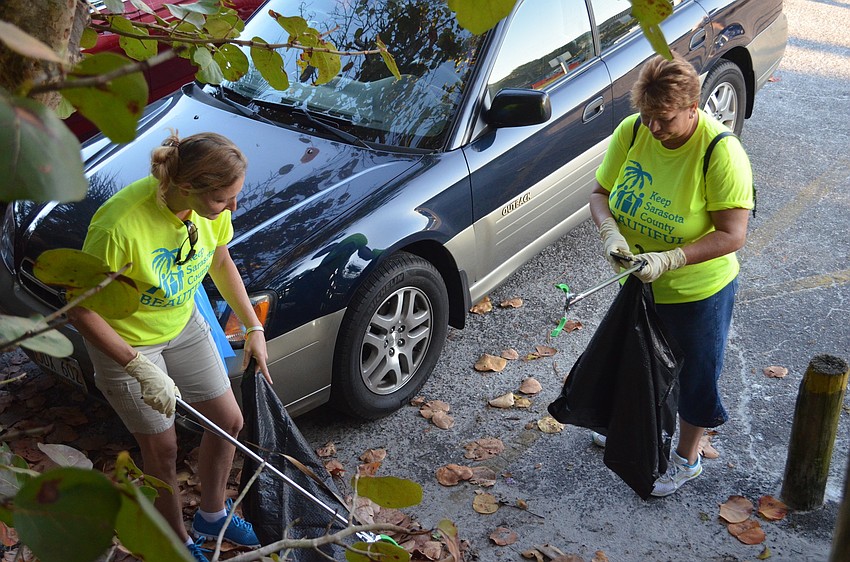 Terry Shuebel and Siesta Key Chamber of Commerce Executive Director, Debra Lynn-Schmitz comb through the parking lot and shrubs.