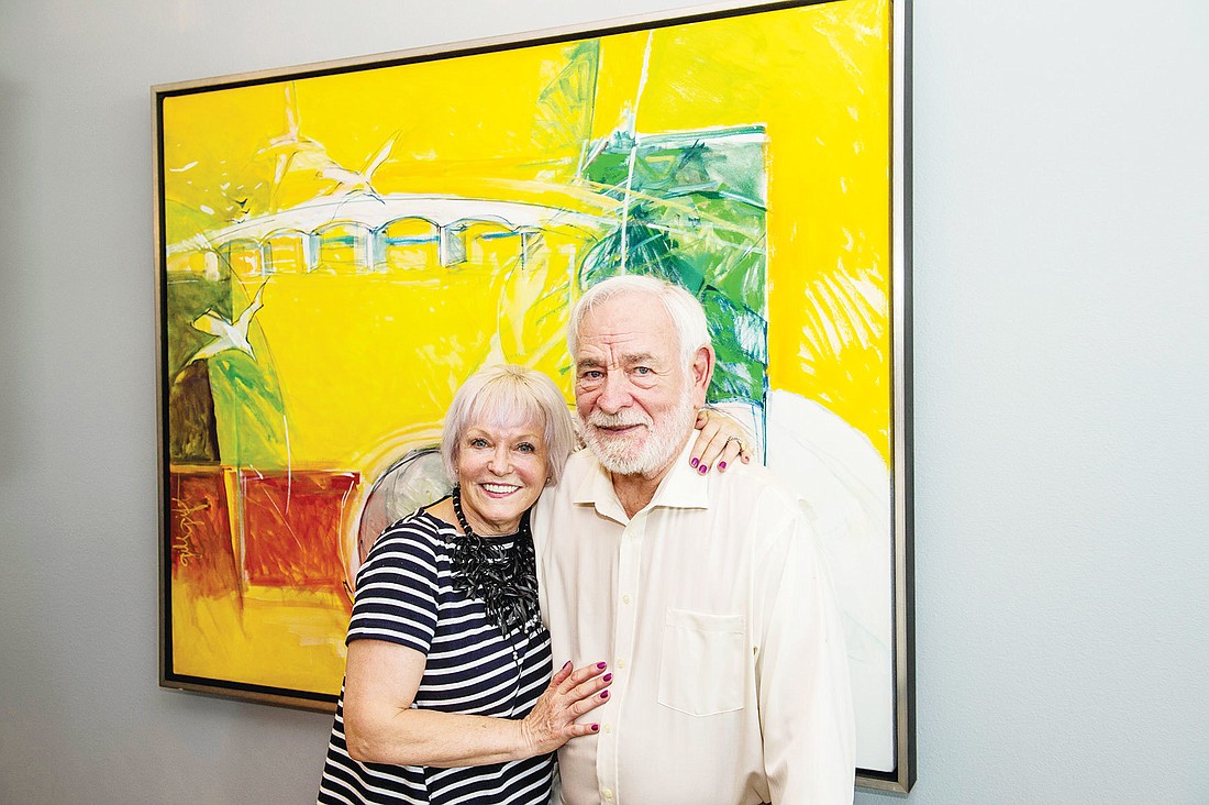 Elisabeth and Gil Waters with Craig Rubadouxu2019s painting of the Ringling Bridge, which also includes the Watersu2019 French bulldog Mimi and cat Kitty. Photo by Cliff Roles.