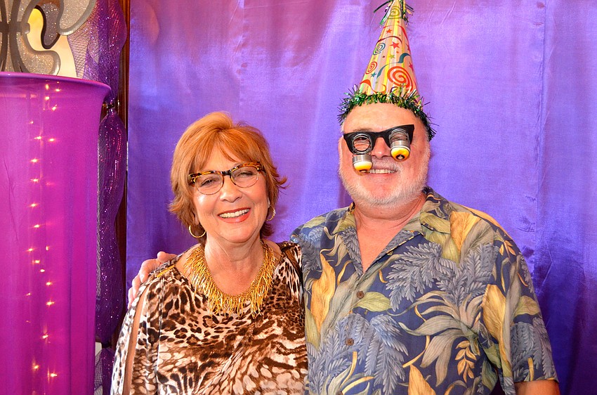Barbara Peat and Dr. Joseph Rich pose with props in front of Mardi Gras-themed backdrop.