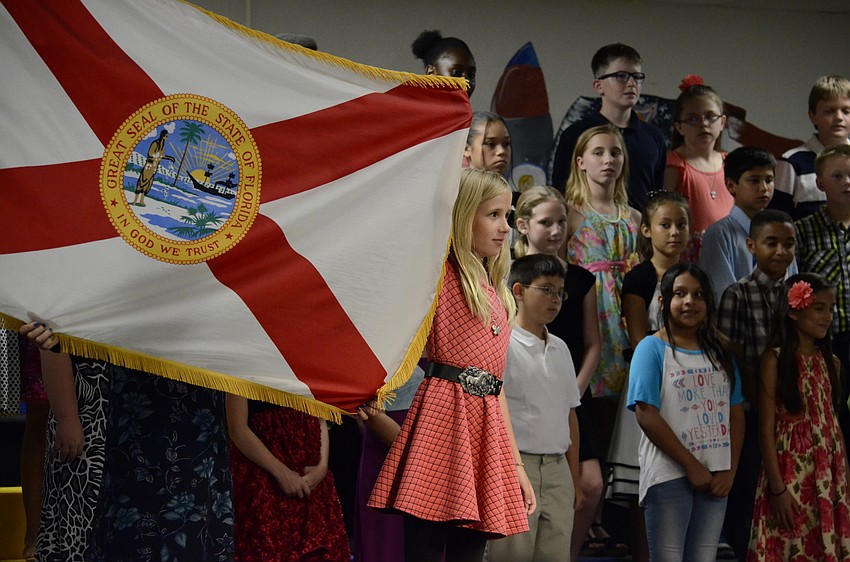 Julia Price holds up the Florida State flag while another student explains the symbolism behind it.