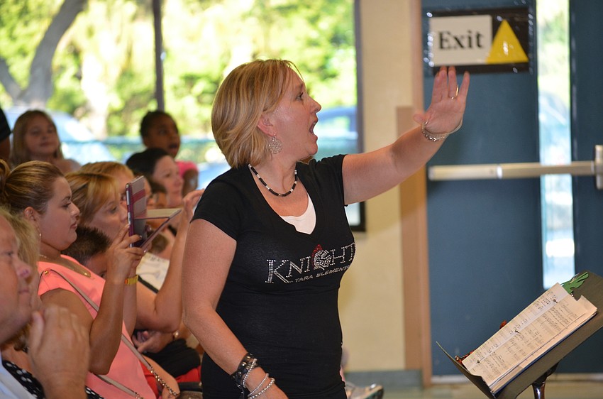 Choir teacher Barbara Siffermann leads her singers in front of the crowd.
