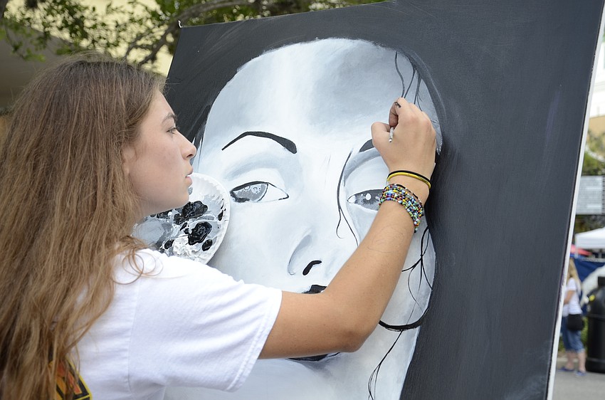 Eighth-grader Rheana White puts the finishing touches on her painting, which was auctioned off. She said the woman in her piece was not based off of anyone.