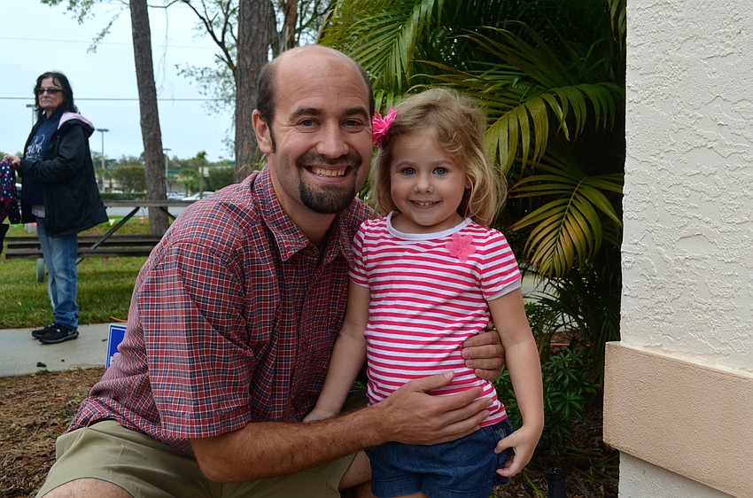 Kersten Schroeder and his daughter, Braelyn, stay dry under the cover of the preschool building.