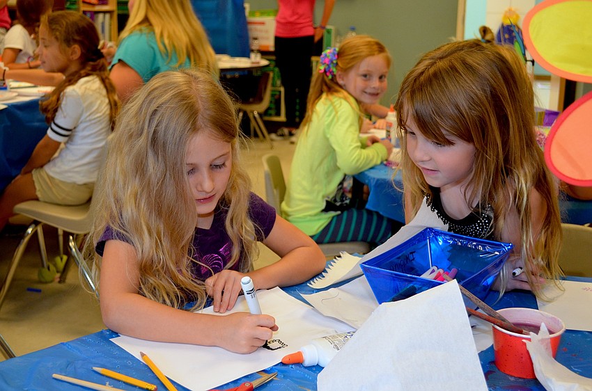 Keira Gagnon colors a necklace with markers as her friend, Olivia Kruse, watches nearby.