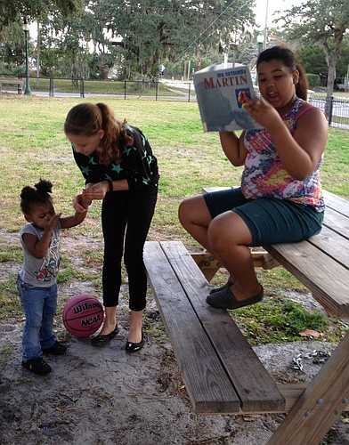 Central-Cocoanut neighborkid Tatiana Johnson, 11, reads at Mary Dean Park as her sister Honestey, 2, and her cousin Camille Homer, 13, listen.