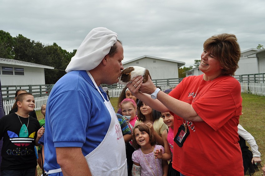 Principal Steve Royce kisses a guinea pig named Twix, as Sheila Waid holds the animal in front of students.