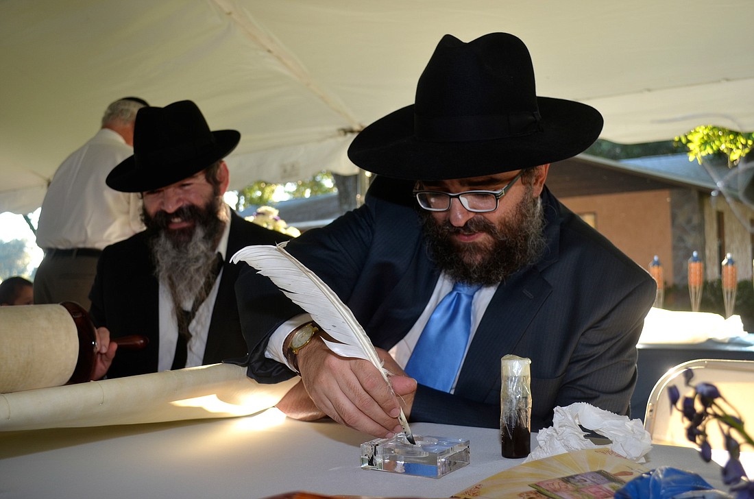 Nochshon Mendel Alvarez watches as Rabbi Yossi Srugo prepares to etch a letter in the Torah.