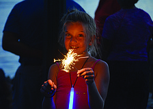 Kayla LeBlanc lights a sparkler at the downtown Fourth of July parade.