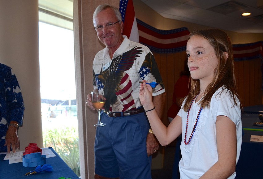Caroline Bell, 11, throws a dart at red and white balloons at a game booth.