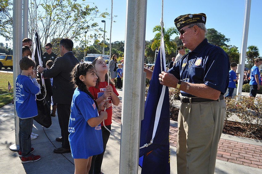 agdalena Morales and Analisa Folsom, behind, raise the Merchant Marine flag with Ret. Army Sgt. Denny King, of Braden River VFW Post 12055.