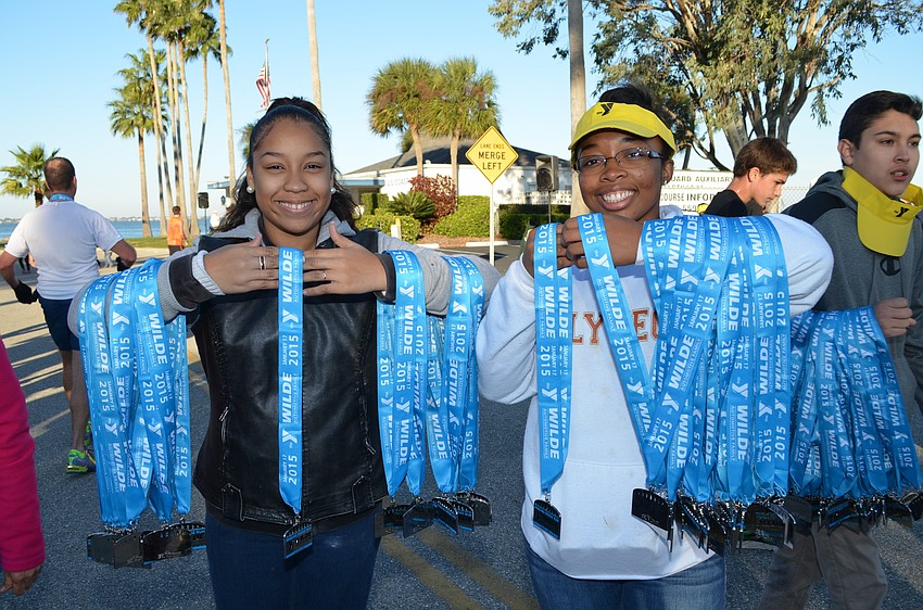Maria Rodriguez-Sanchez and Nicole Eddins help pass out participation medals as runners cross the finish line.