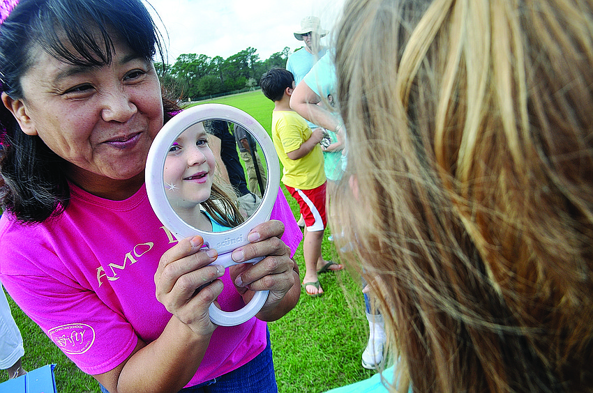 Face-painting artist Akiko Campbell shows Abigail Pfeiffer, 6, the rainbow on her face.