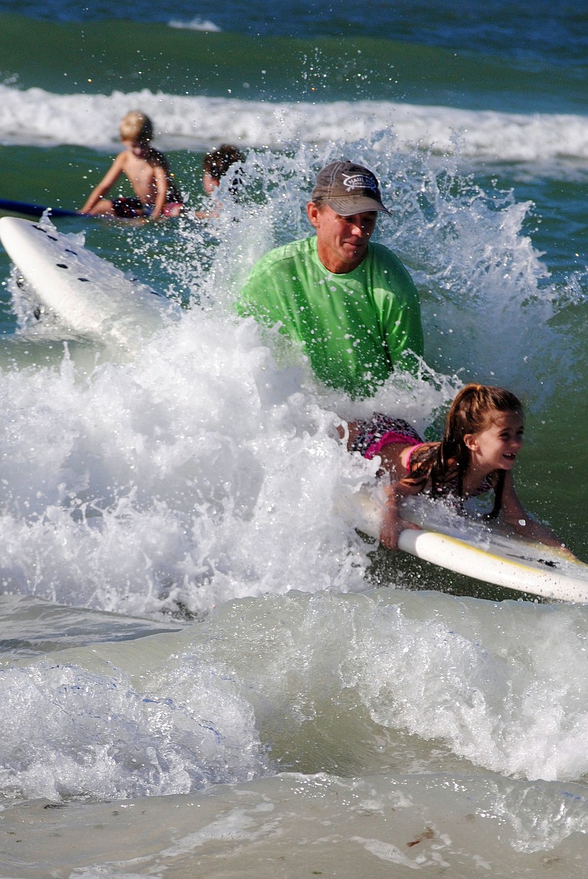 A young surfer catches a wave with the help of a volunteer.
