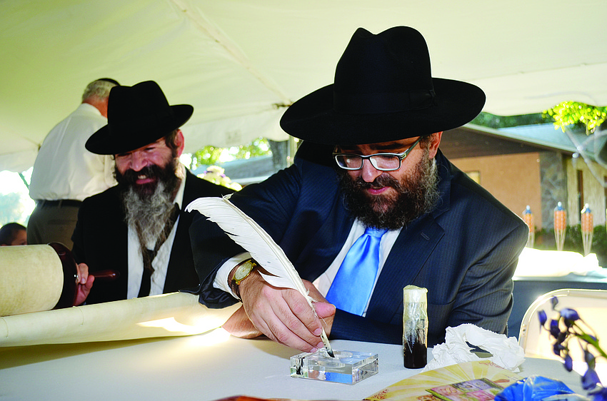 Nochshon Mendel Alvarez watches as Rabbi Yossi Srugo prepares to etch a letter in the Torah as Chabad of Bradenton celebrates Manatee County's first dedicated Torah handwritten by a scribe in Israel.