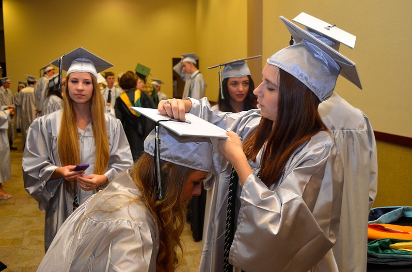 Meghan Neu waits while Michele Bohlmann adjusts her graduation cap.