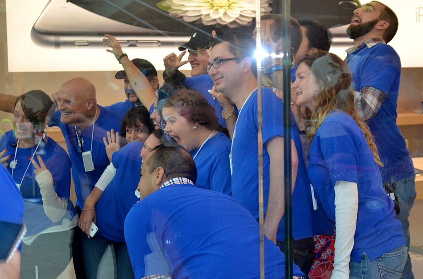 Apple store employees wave to shoppers who anxiously waiting for the store to open.
