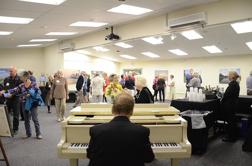 Billy Marcus plays the piano for around 40 attendees who trickled in and out of the exhibit, admiring Louis Cabot's canvas prints.