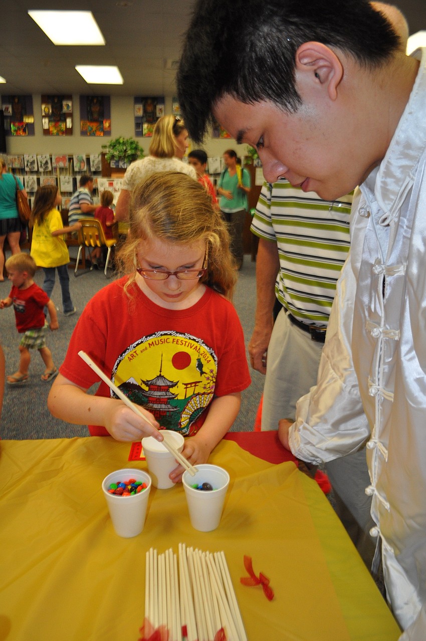 Rowan Gould learns to use chop sticks with the help of Braden River High School Chinese Club member Kevin Lai.