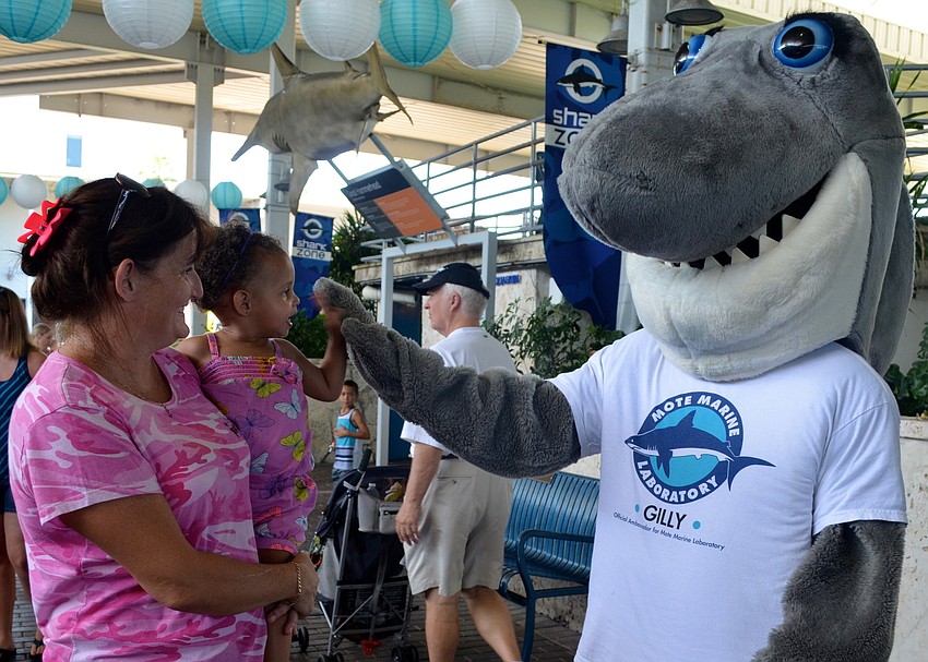 Lisa Keith holds Olivia Bell, 2, as she gives Gilly the Shark a high-five.