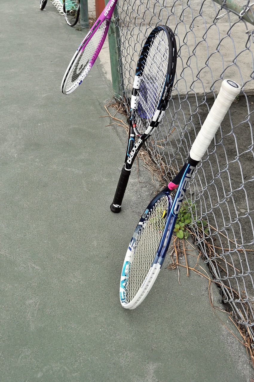 Kids leave their racquets on the fence while they stretch.