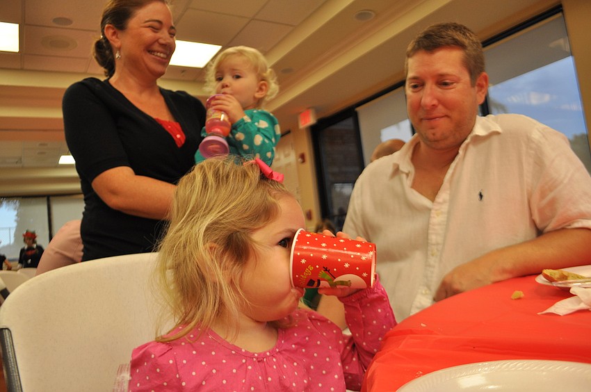 Leah Glynn takes a drink of orange juice as her family watches. Pictured are mom and dad, Shawna and Dave, and sister, Lauren.