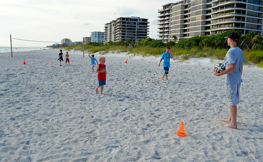 A group of children play soccer on the beach while the adults enjoy dinner.