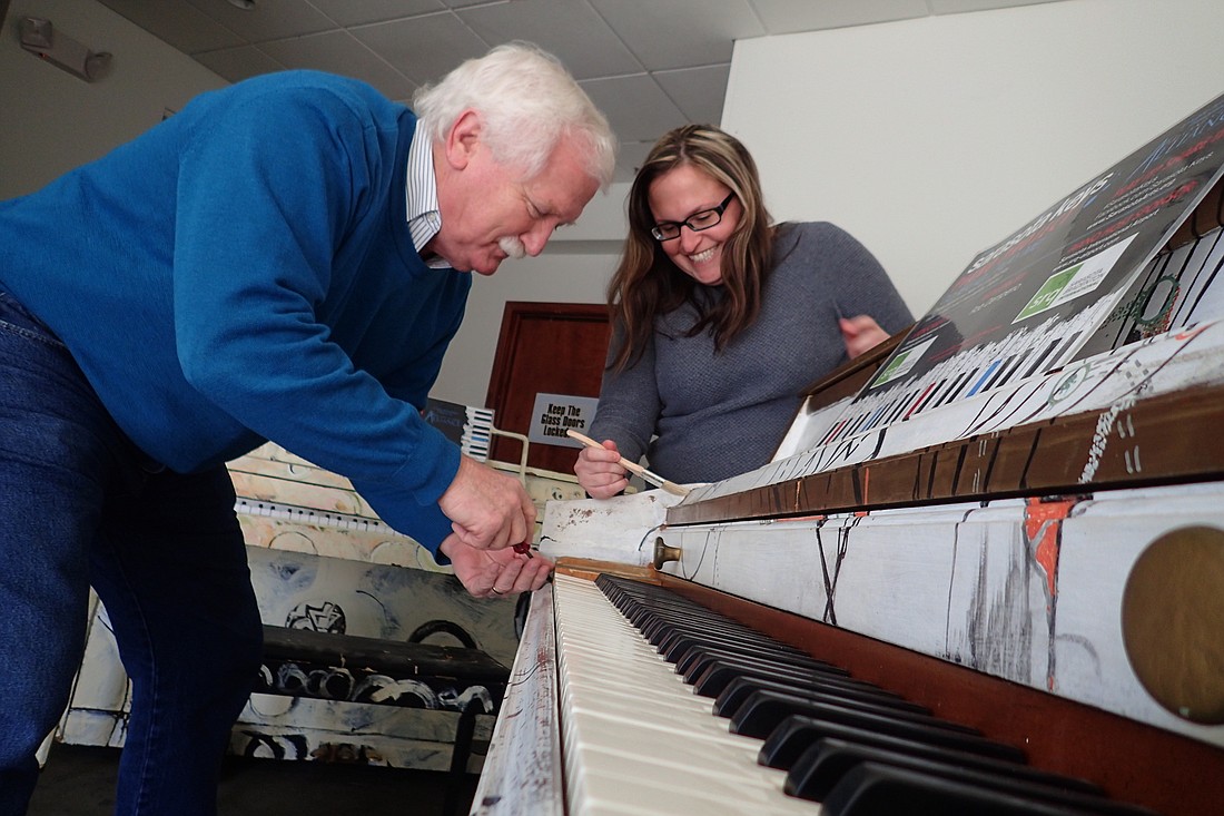 Arts Alliance Executive Director Jim Shirley and Communications Manager Rachel Denton apply finishing touches to artist Robert Demperio's piano, "A Classical Response to Experimental Composition."