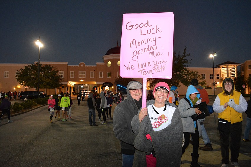 Patti Prince of Bradenton holds the sign that was made for her by family and friends. David Koppin of Palmetto, standing just behind her, was among the support group to watch her first half marathon.