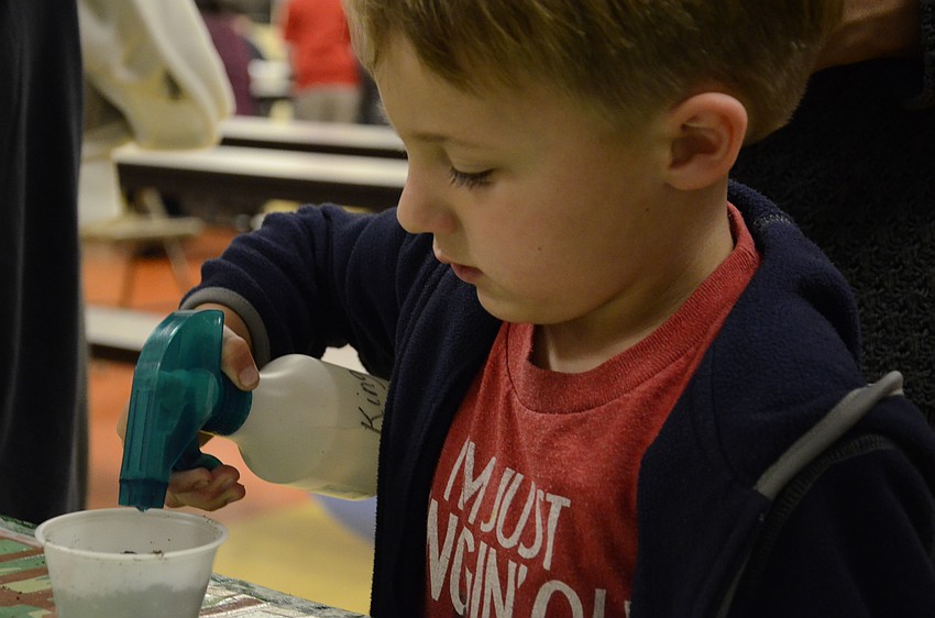 Logan Walker sprays water onto his cup of planted seeds.