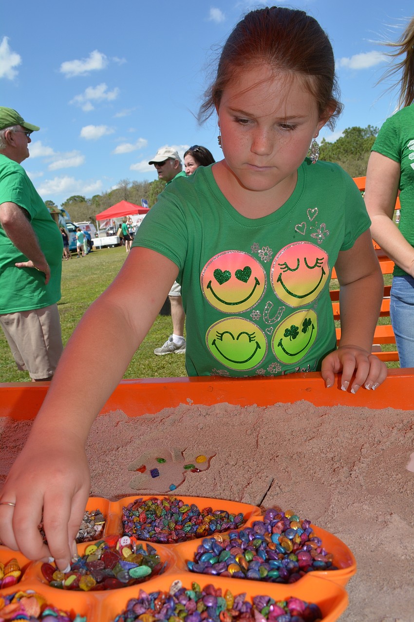 Ava Filewich, a student at McNeal Elementary, selects stones and shells to decorate a sand-cast shamrock.