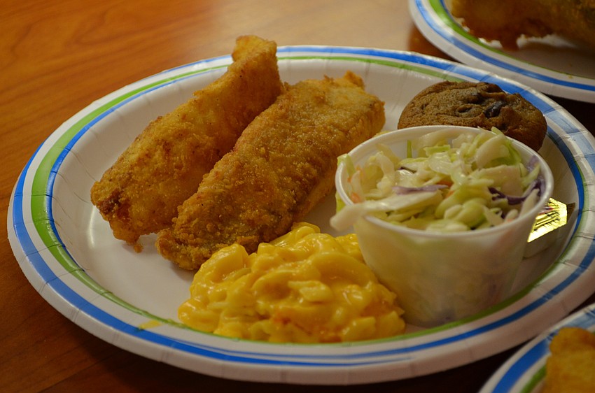 The meal includes two pieces of fried white fish, cornbread, coleslaw, macaroni and cheese, a drink and a chocolate chip cookie for dessert.
