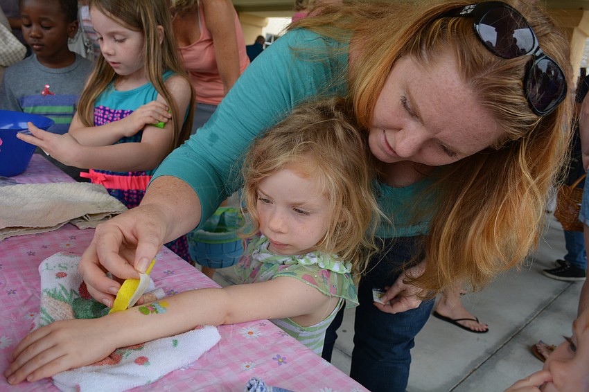 Ashley Pressinone helps her daughter, Alexa, put on a temporary frog tattoo.