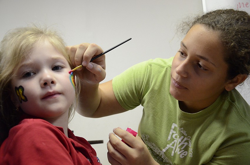 Sami Copeland paints a rainbow heart onto Addy Hartley's cheek.