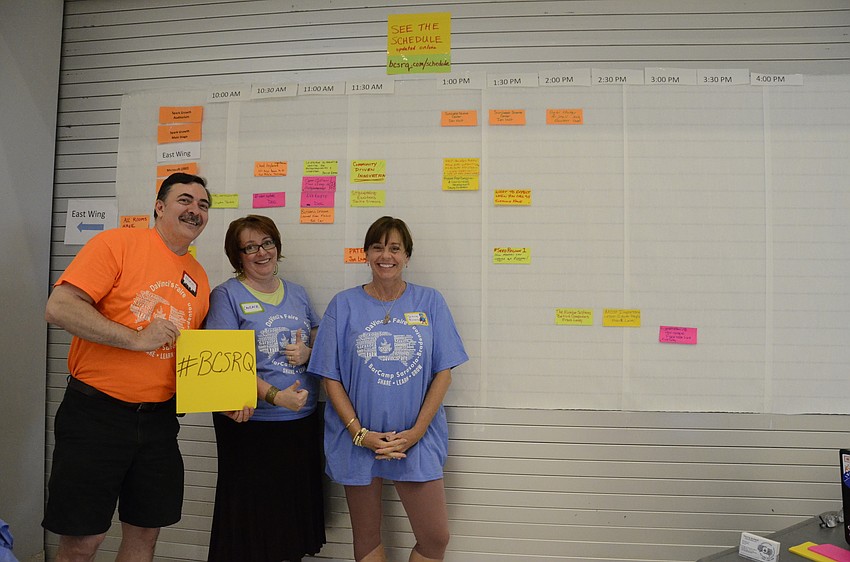 Volunteers Norm Dempsey, Candace Lourdes and Diane Rivers help with the speaker schedule board — anyone attending could sign up to speak about a topic of their choice.