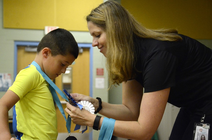 Olga Wolanin with Manatee County pins first-grader Dylan Neuweiler with his first place ribbon.