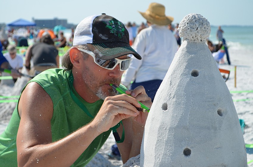 Bruce Peck blows grains of sand from the cap of his creation 