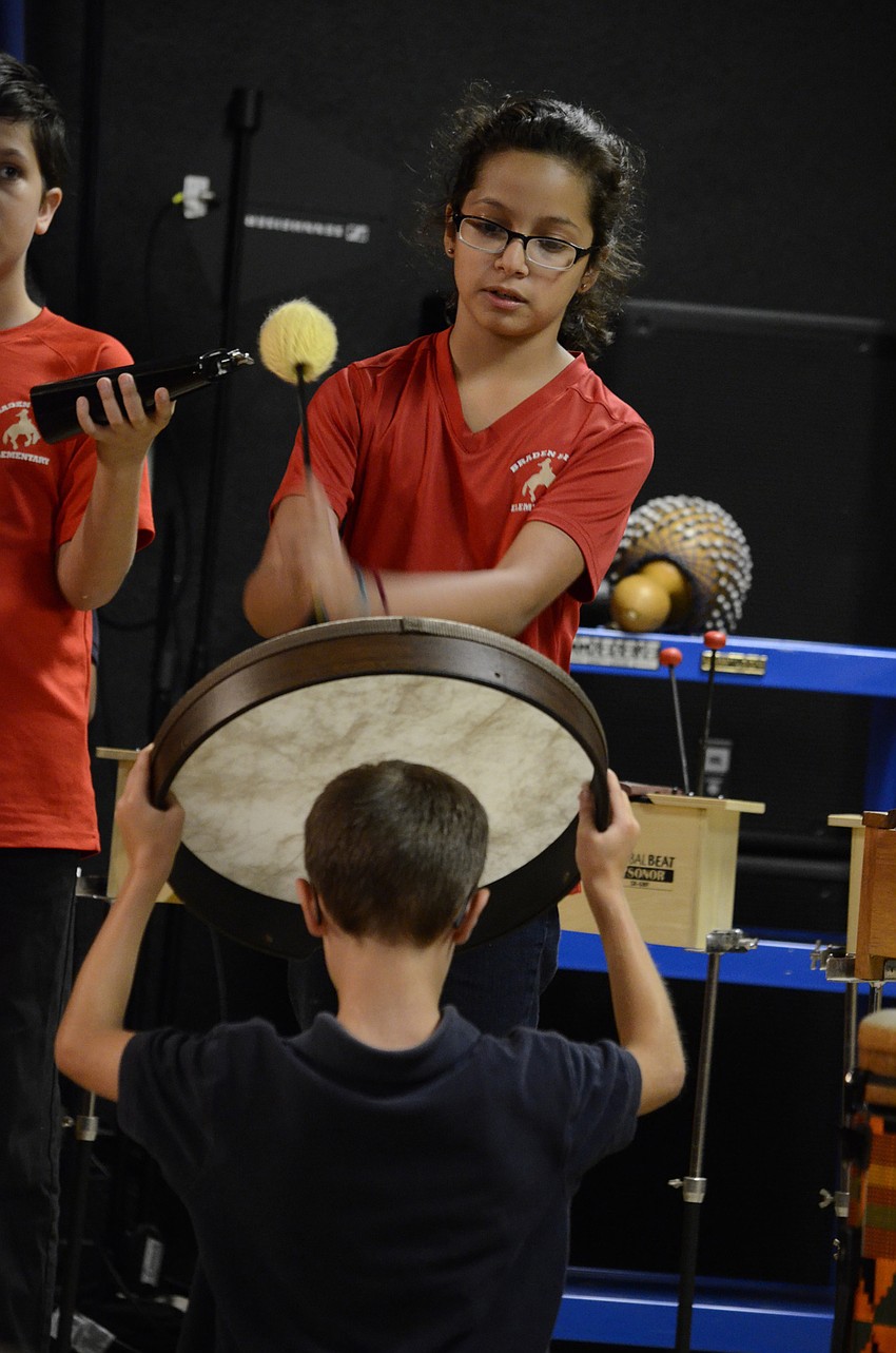 Niley Molina beats a frame drum, and John Emposimoto holds it up.