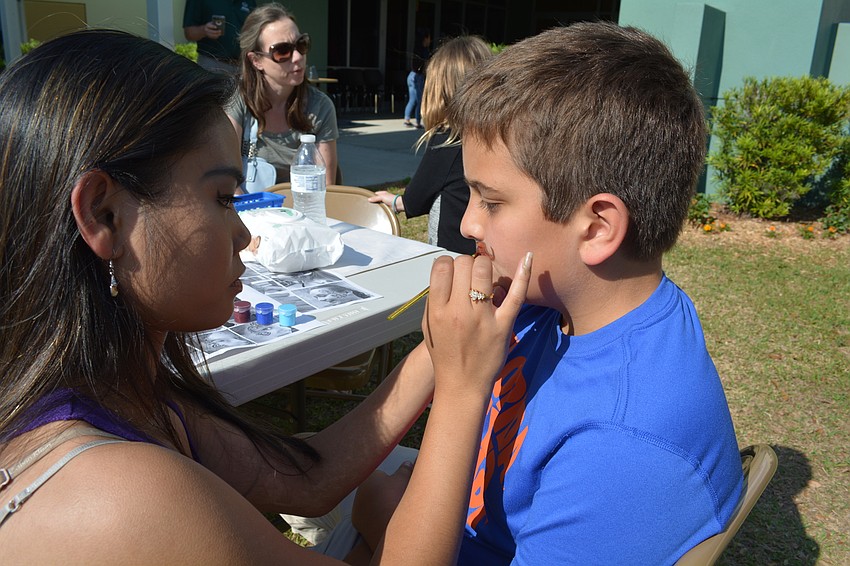 Lakewood Ranch High's Alexa Tadelman paints a mustache on the face of 10-year-old Andrew Boudreau.