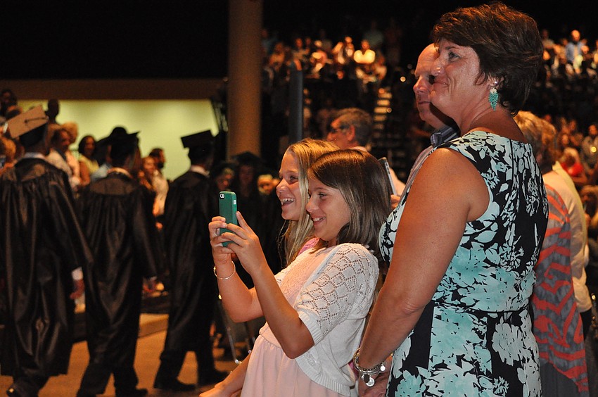 Lisa Zona and twins Sara and Amy Zona video their older brother, Derek, as he enters the ceremony.