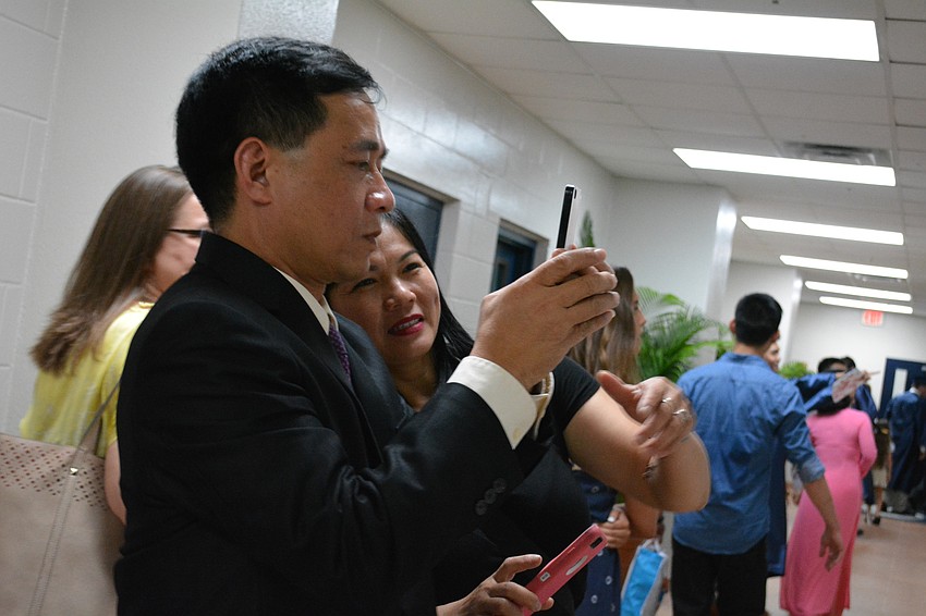 Tung Hoang and his wife Thanh Nguyen, not pictured, came from Vietnam to watch their son, Nam, graduate. Tung Hoang snaps a photo of his son's senior portrait hanging in the hallway. Nam Hoang's aunt, Giang Geringer looks over his shoulder.
