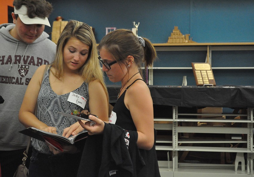 Former students Vincent Kersey, Shelby Egan and Diana Mastrangelo flip through a yearbook.