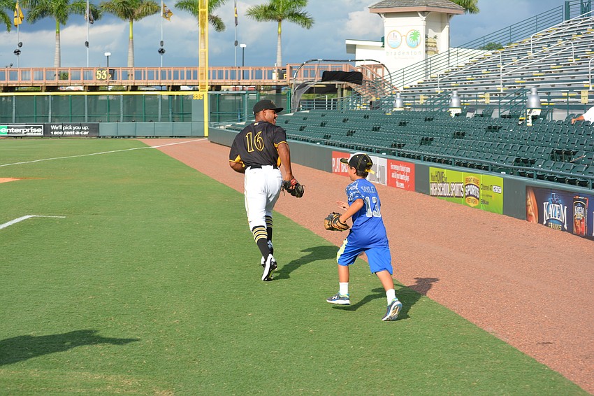 Marauders outfielder Elvis Escobar urges Manatee's Brandon Samler to keep up as they run to his position before the game.