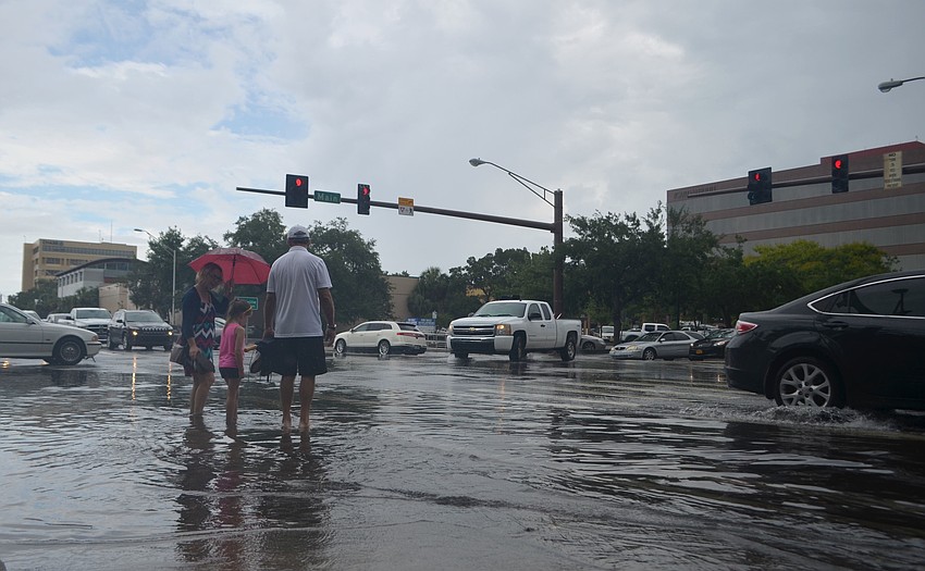 Nicole Fallon (left) waits to cross the intersection of Main Street and Washington Boulevard with her daughter, Corrine Dubois (center) and father, Walt Fallon (left), Tuesday, June 7 in Sarasota, Florida. The intersection flooded in the early afternoon.