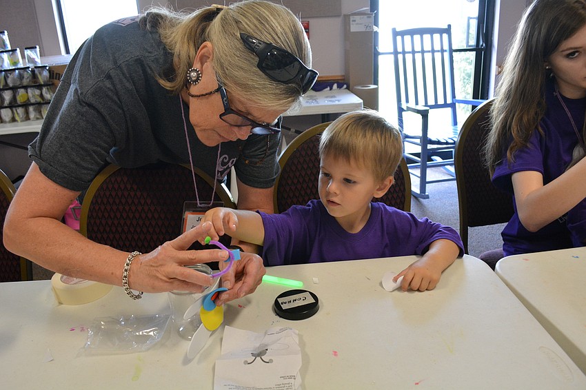 Volunteer Jody Jorgensen helps Conrad Manuel, 3, make a lightning bug craft.