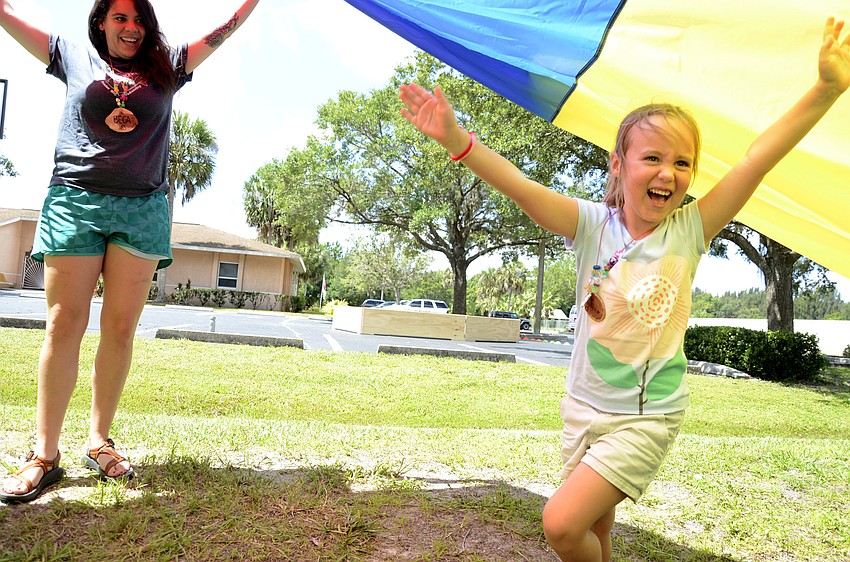 Day camp director Beca Franca holds up the parachute as Noelle Stead runs through.
