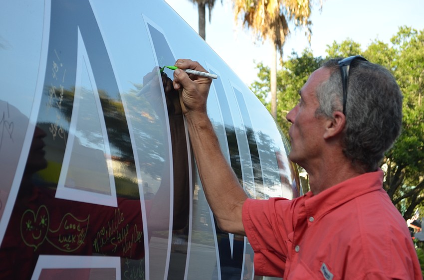 Doug Matejka signs his name to the Alex and Ani boat.
