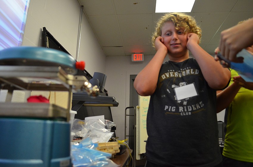 Eitan Campbell covers his ears and watches as his sculpture is pressed into a mold.