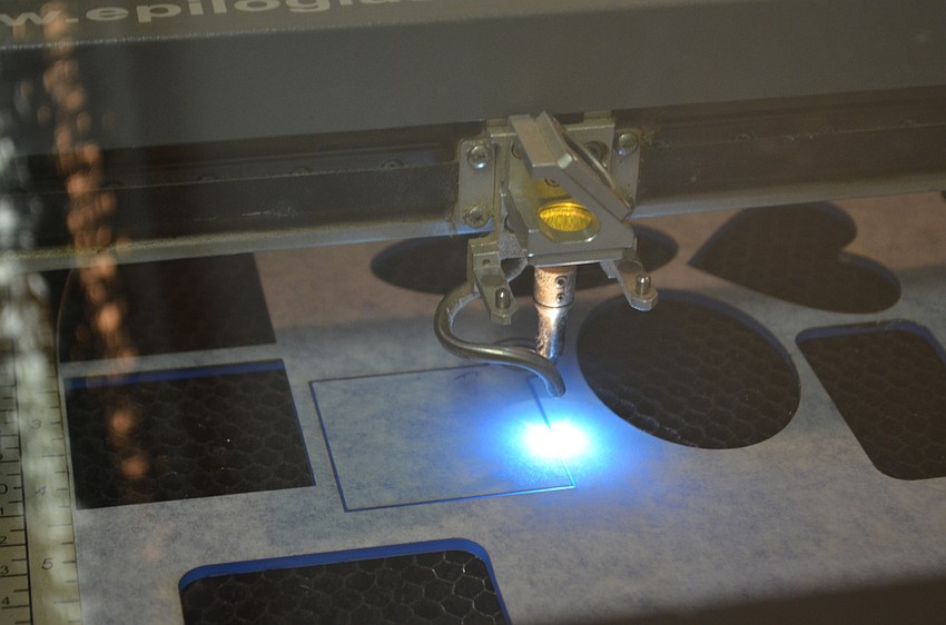 A laser cutter outlines the design for an acrylic keychain.